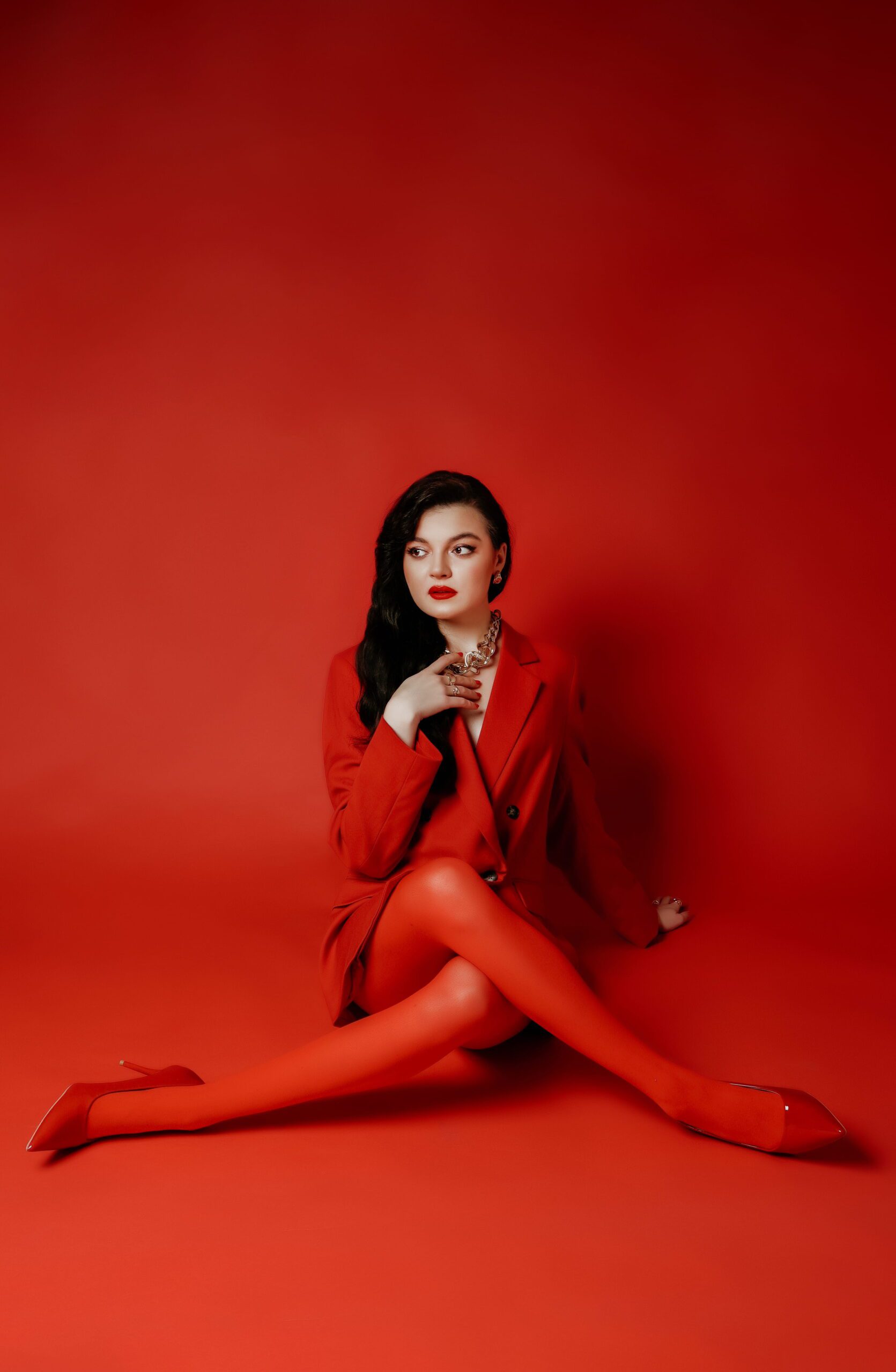 A woman sitting in a vivid red outfit against a red background