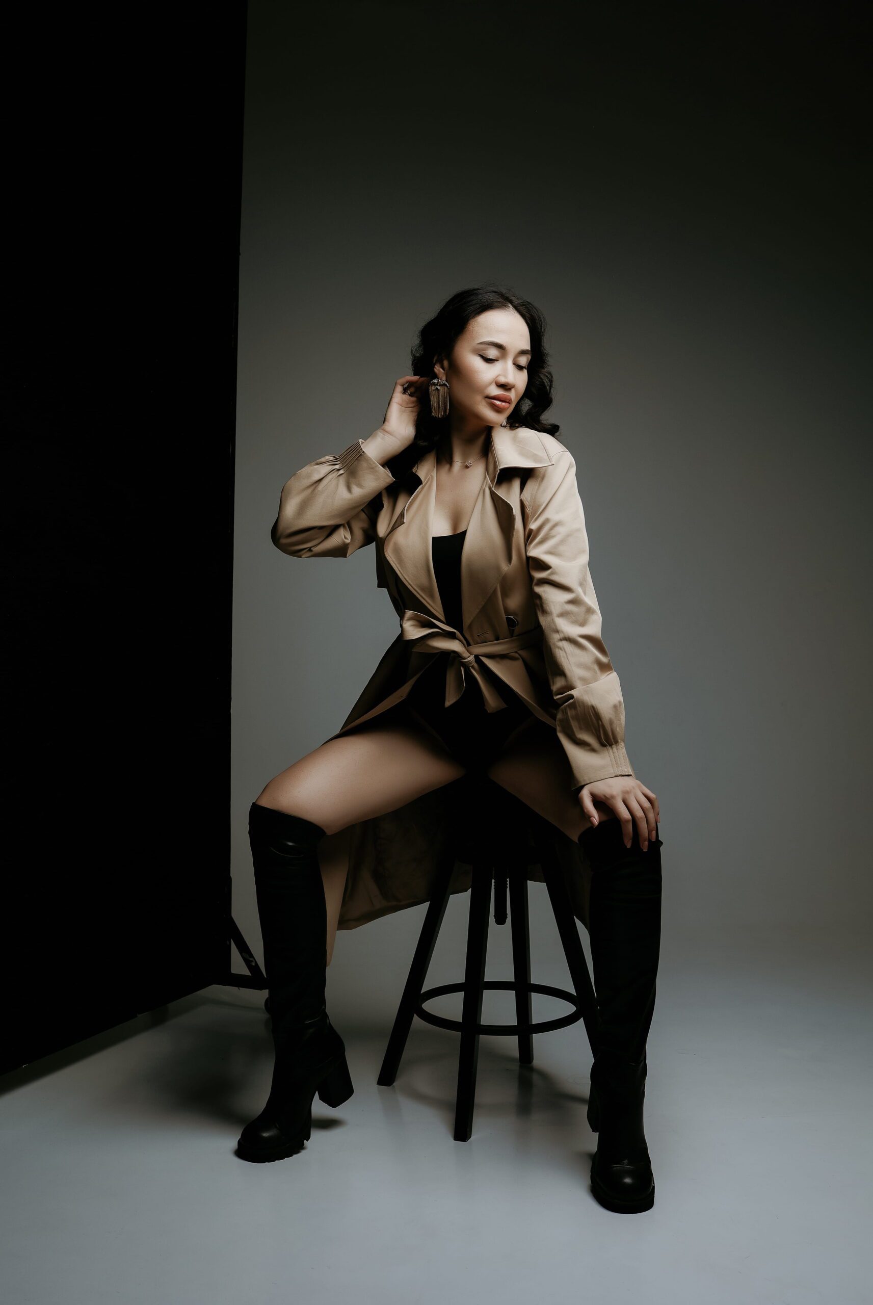 A woman seated in a tan jacket in a softly lit studio