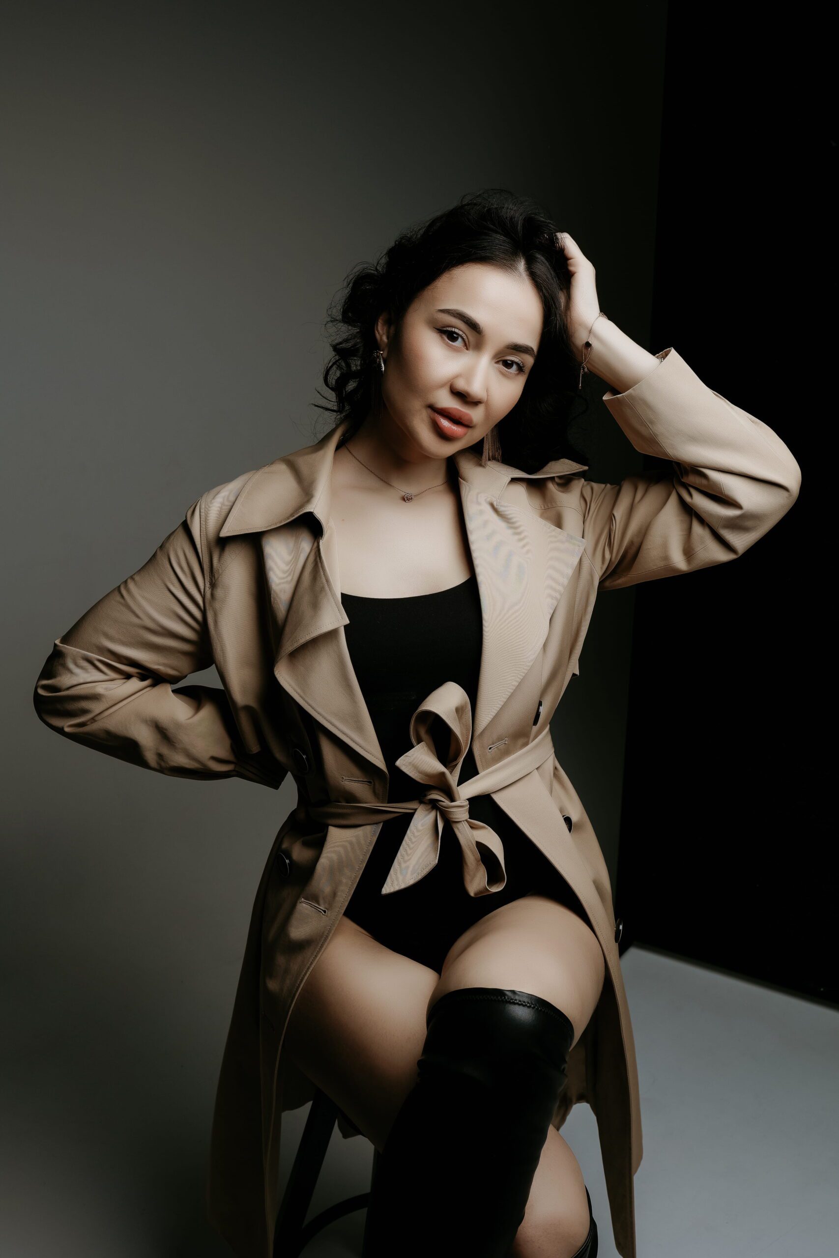 A woman in a tan jacket with one hand in her hair