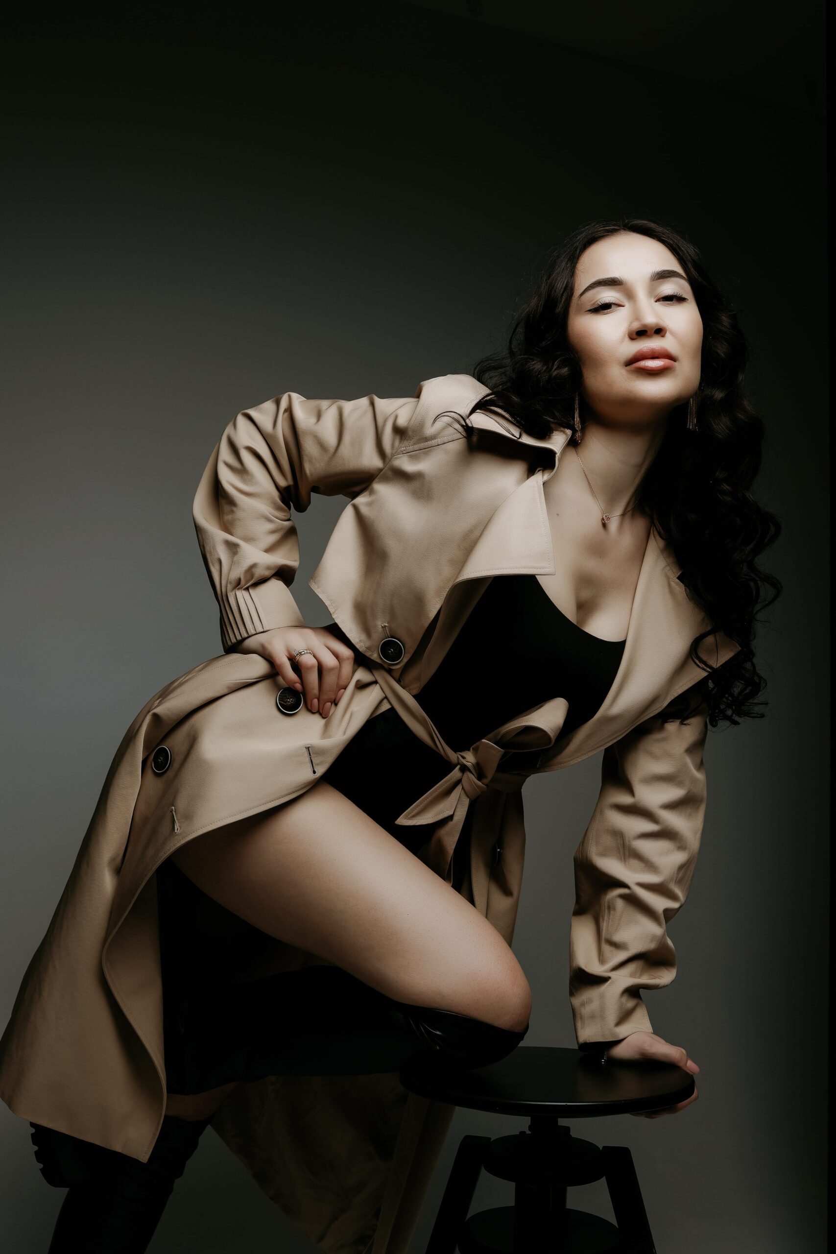 A woman in a tan jacket seated beneath studio lighting