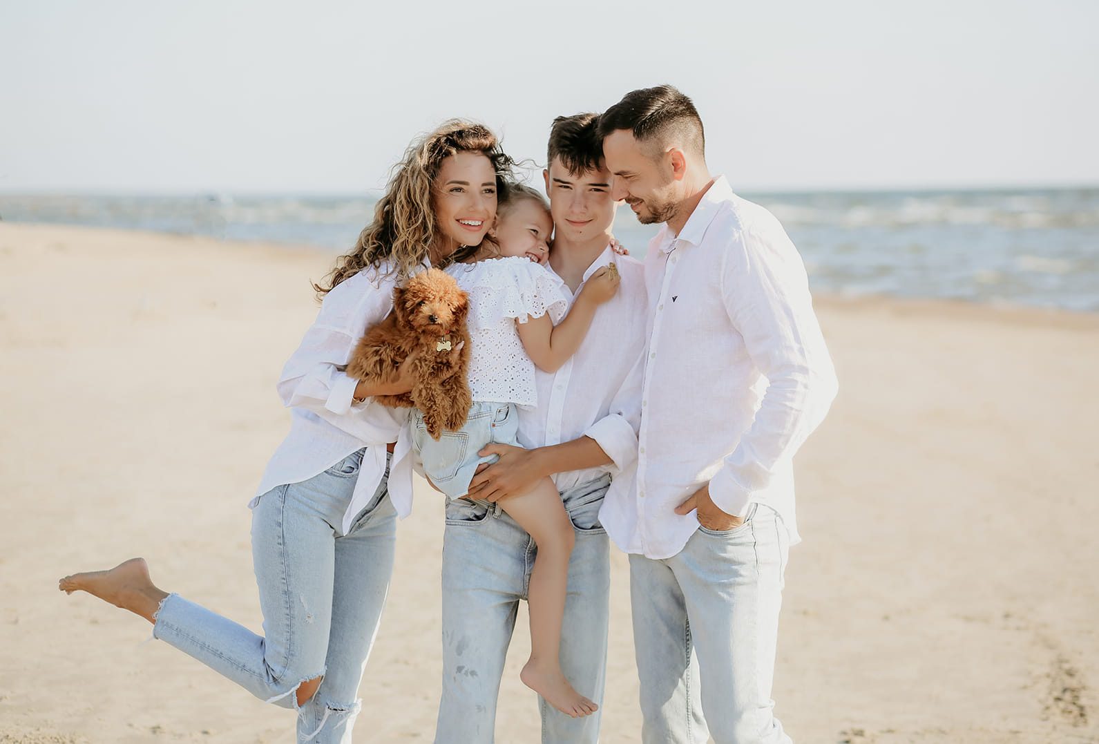A family holding their dog close on a sunlit beach